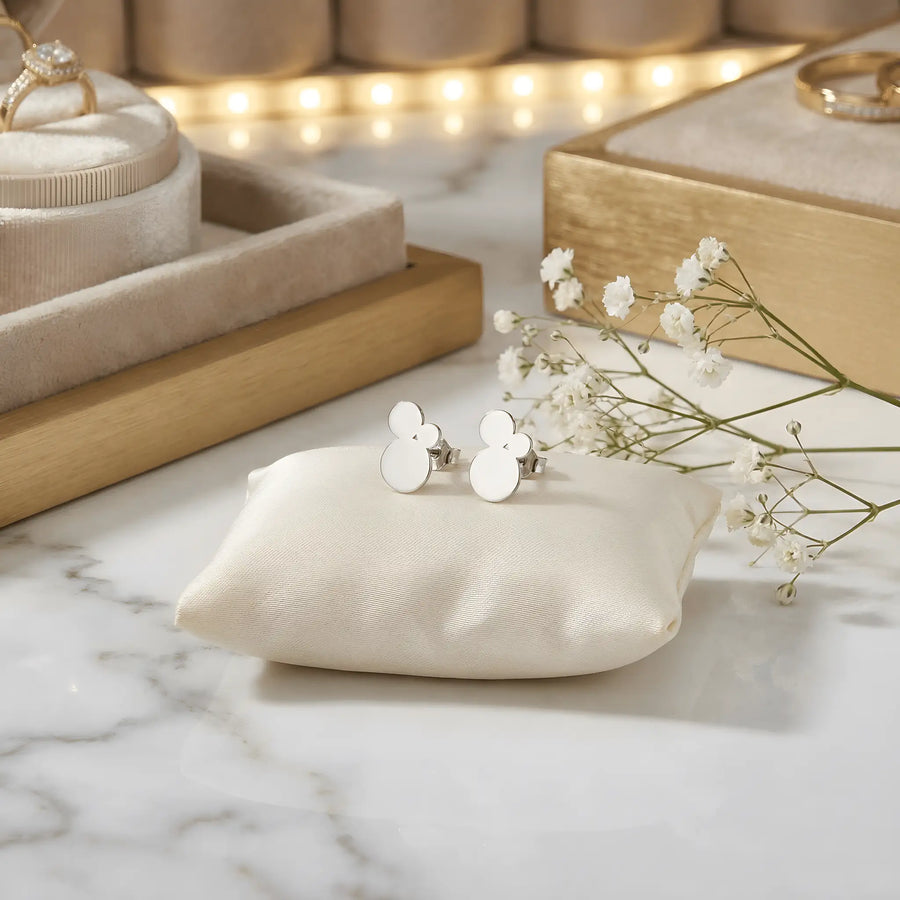 Cercei argint 925 rodiat stud cu trio cercuri pline suprapuse 11,6mm — pereche pe pernă satin crem cu placă marmură albă cu vinete gri, cutii bijuterii din lemn auriu și flori gypsophila pe fundal cu lumini bokeh aurii, finisaj oglindă alb-platinat, prindere fluturaș clasic