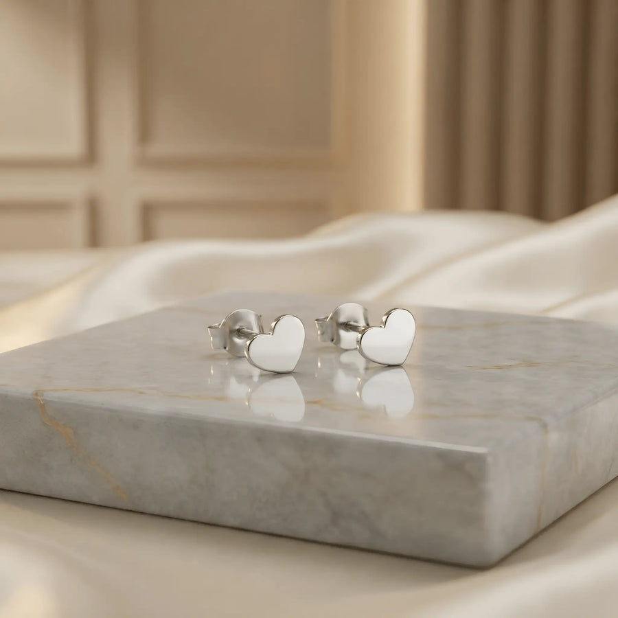 Cercei argint 925 rodiat stud cu inimă plină 9x8mm — pereche pe placă de marmură albă cu vinete aurii pe fundal crem cu draperie satin, finisaj oglindă alb-platinat, prindere fluturaș clasic, tijă 10,5 mm