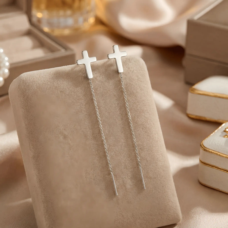 Cercei argint 925 rodiat threader cu cruce latină mică 6,5mm — pereche pe pernă velvet bej cu draperie satin crem și cutii de bijuterii cu margini aurii în fundal, lanț subțire 6cm cu tijă-bară, finisaj oglindă alb-platinat