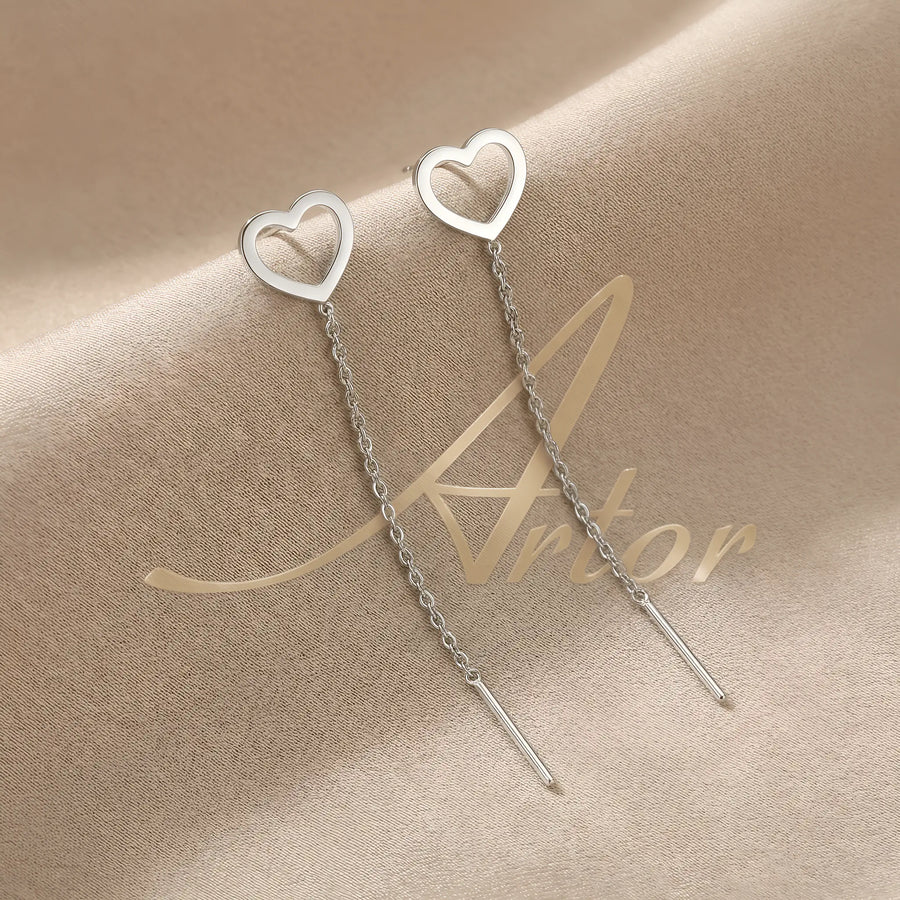 Cercei argint 925 rodiat threader cu inimă outline 8mm — pereche pe satin auriu cu logo Artor pe fundal, contur subțire al inimii cu interior gol, lanț subțire 6cm cu tijă-bară, finisaj oglindă alb-platinat