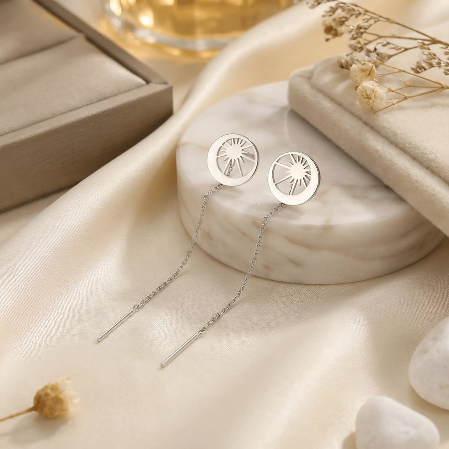 Cercei argint 925 rodiat threader cu disc lună-soare 10mm — pereche pe placă marmură albă rotundă cu satin crem și flori uscate gypsophila pe fundal, decupaj soare cu raze și arc lunar lateral, lanț subțire 6cm cu tijă-bară, finisaj oglindă alb-platinat