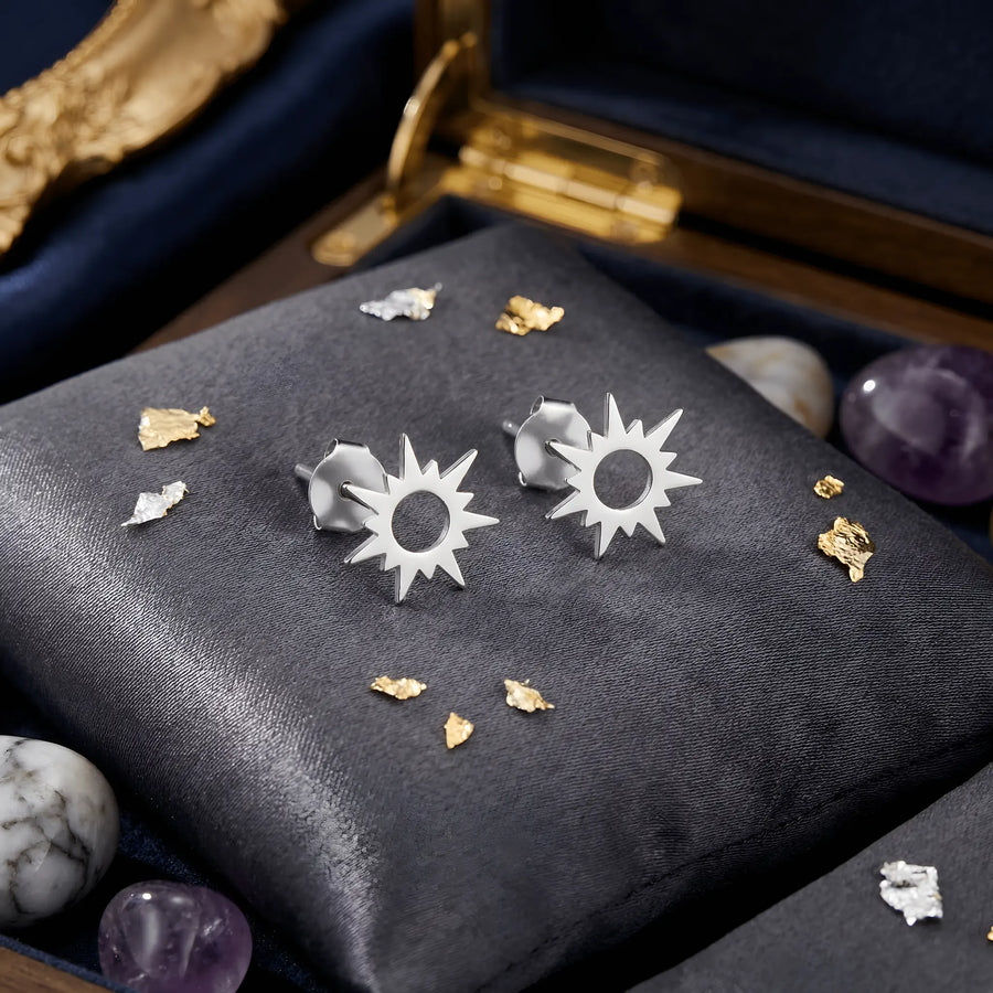 Cercei argint 925 rodiat stud cu soare stilizat 10x10mm — pereche pe pernuță gri-velvet cu pietre de cristal de stâncă, ametist și fragmente aurii decorative, cutie de bijuterii cu detalii aurii pe fundal, finisaj oglindă alb-platinat