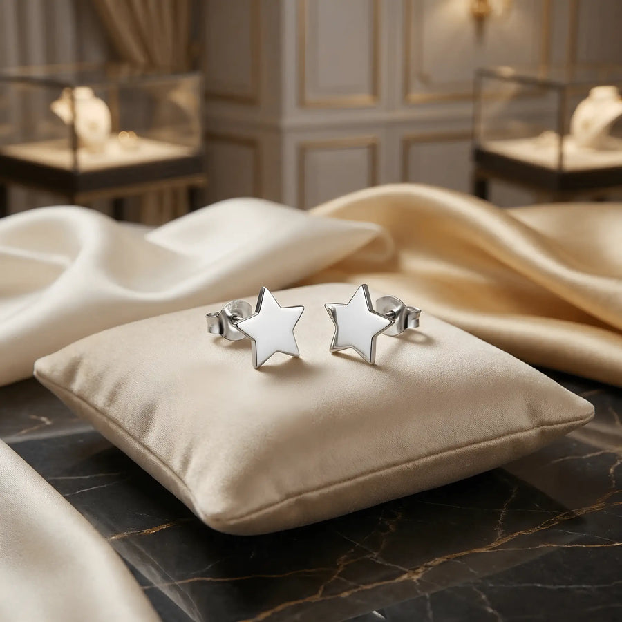 Cercei argint 925 rodiat stud cu stea cu 5 colțuri plină 9x8.5mm — pereche pe pernuță crem cu marmură neagră lăcuită cu vene aurii, vitrine bijuterii pe fundal, finisaj oglindă alb-platinat, prindere fluturaș push-back