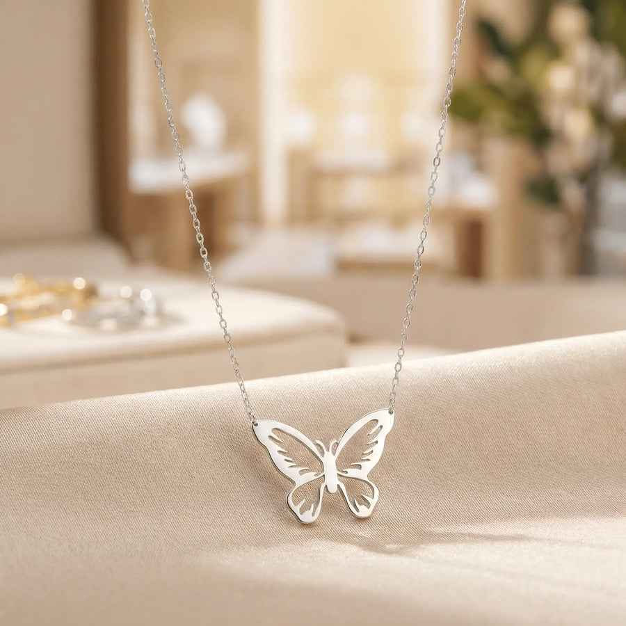 Lănțișor argint 925 rodiat cu pandantiv fluture cu aripile larg desfăcute și motive decupate fin pe lanț subțire alb-platinat, ambianță atelier crem