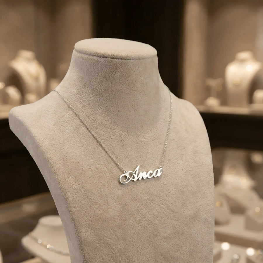 Lănțișor argint 925 rodiat personalizat cu numele Anca decupat în scriere cursivă elegantă cu A buclat pe bust display gri velvet în showroom, lanț subțire alb-platinat