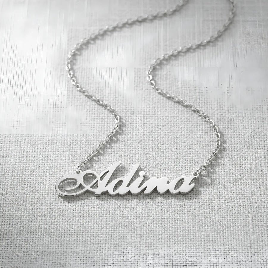 Lănțișor argint 925 rodiat personalizat cu numele Adina decupat în scriere cursivă elegantă cu coadă caligrafică pe textil alb țesut, lanț subțire alb-platinat
