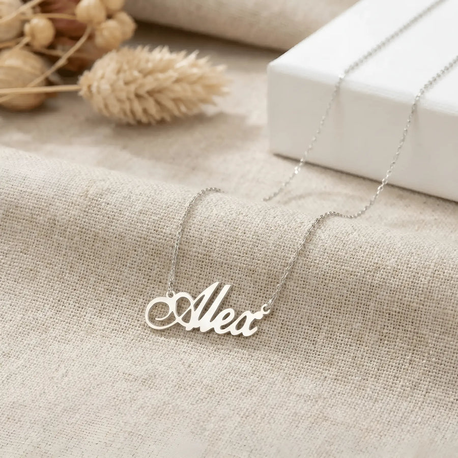 Lănțișor argint 925 rodiat personalizat cu numele Alex decupat în scriere cursivă elegantă cu coadă caligrafică pe textil bej cu cutie albă, lanț subțire alb-platinat