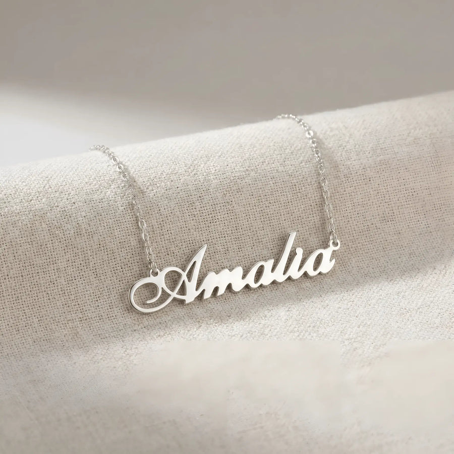 Lănțișor argint 925 rodiat cu numele Amalia, pandantiv decupat 38x10 mm font cursiv inițiala A cu buclă jos-stânga, lanț anchor 46 cm pe textil natural ivory tip in cu pliuri