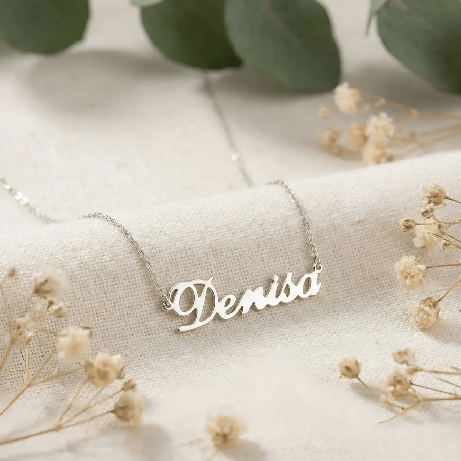 Lănțișor argint 925 rodiat cu numele Denisa, pandantiv decupat 38.5x10 mm font cursiv inițiala D cu curbă închisă, lanț anchor 46 cm pe textil ivory mat cu eucalypt și gypsophila uscată