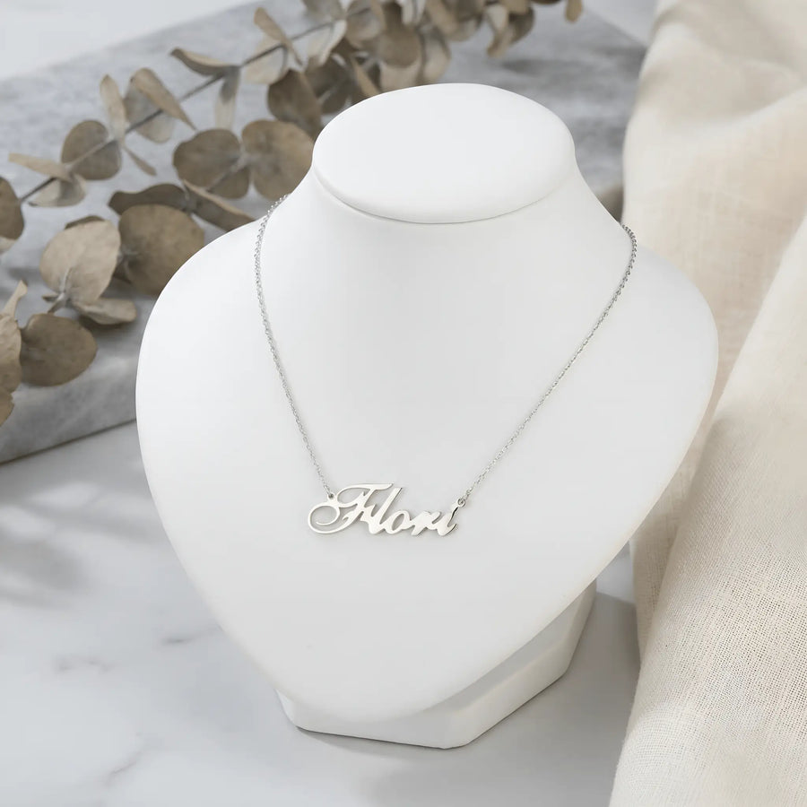 Lănțișor argint 925 rodiat personalizat cu numele Flori decupat în scriere cursivă elegantă cu F și coadă caligrafică pe bust display alb cu eucalipt uscat, lanț subțire alb-platinat