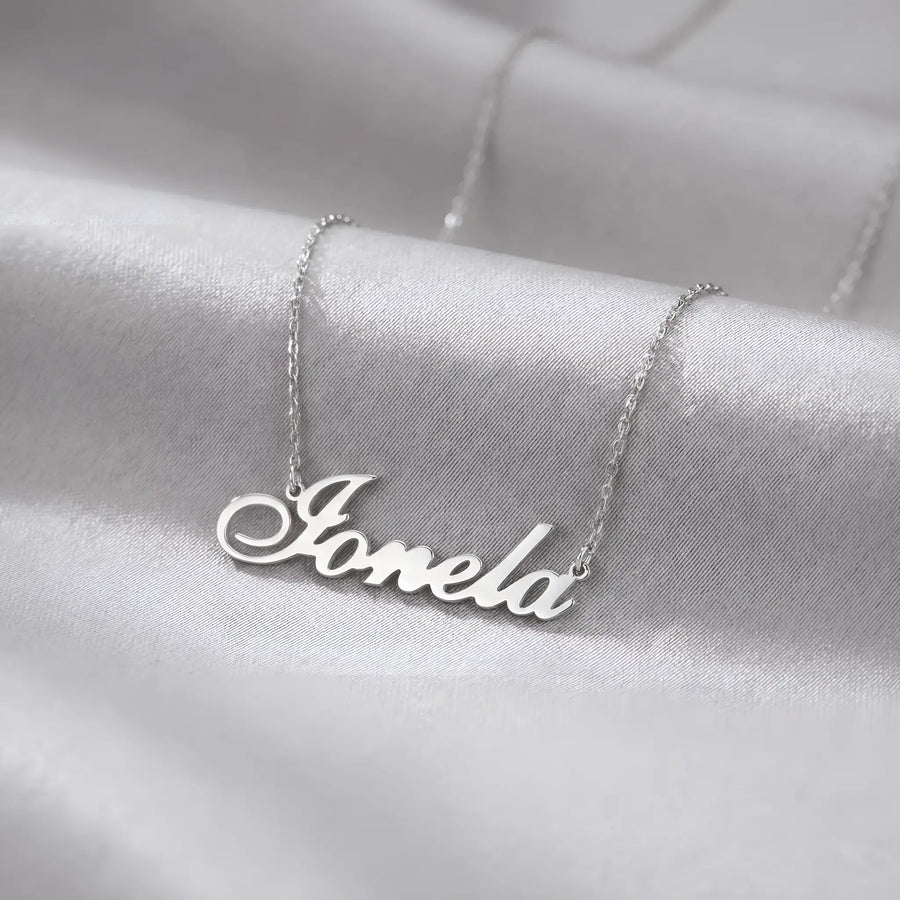 Lănțișor argint 925 rodiat cu numele Ionela, pandantiv decupat 38.5x10 mm font cursiv inițiala I cu coadă subțire descendentă, lanț anchor 46 cm pe textil satinat alb