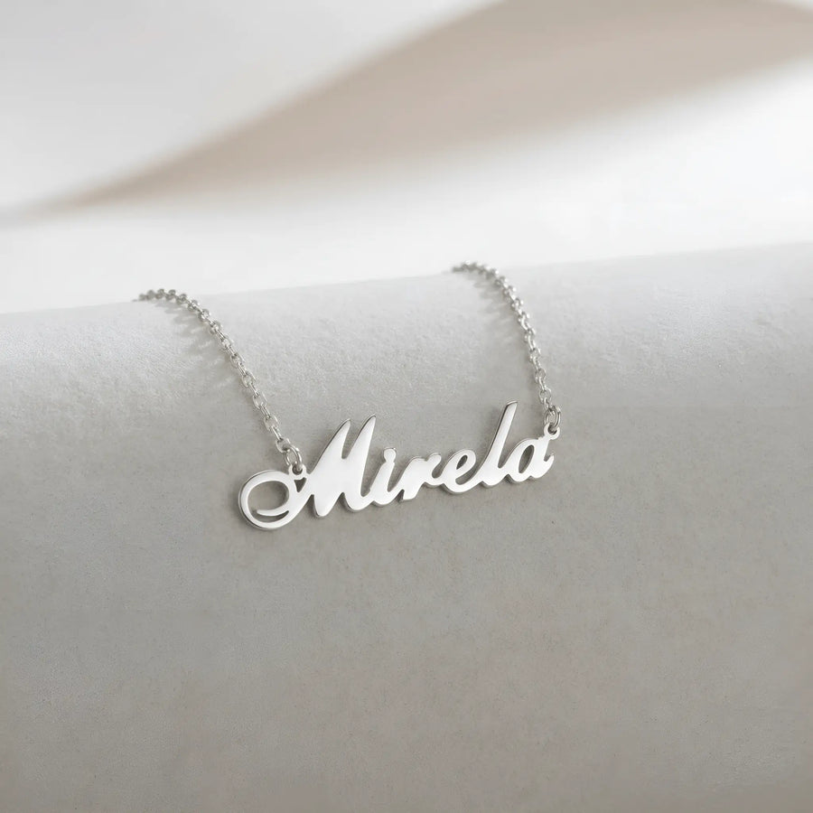 Lănțișor argint 925 rodiat cu numele Mirela, pandantiv decupat 38x10 mm font cursiv inițiala M cu curbă dublă înaltă, lanț anchor 46 cm pe textil natural ivory tip in