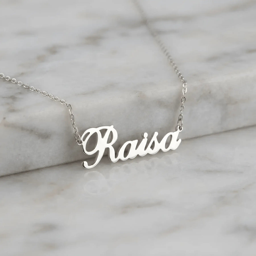 Lănțișor argint 925 rodiat cu numele Raisa, pandantiv decupat 34.5x10 mm font cursiv inițiala R cu buclă jos, lanț anchor 46 cm pe blat de marmură albă