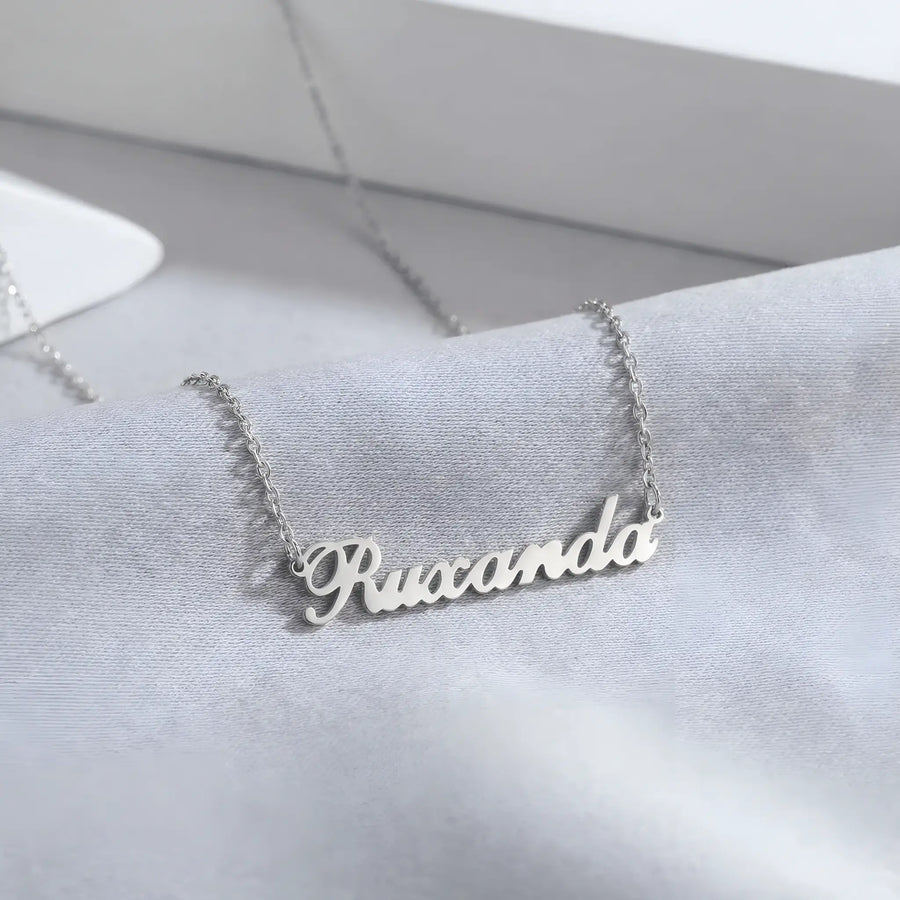 Lănțișor argint 925 rodiat cu nume Ruxanda, caligrafie cursivă decupată pe lanț fin anchor, fundal mătase gri-albastru