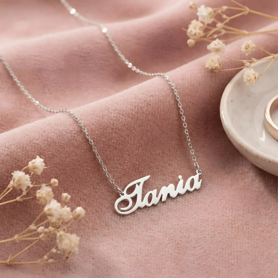 Lănțișor argint 925 rodiat personalizat cu numele Tania decupat în scriere cursivă elegantă cu T cu curbă orizontală pe textil roz cu flori uscate, lanț subțire alb-platinat