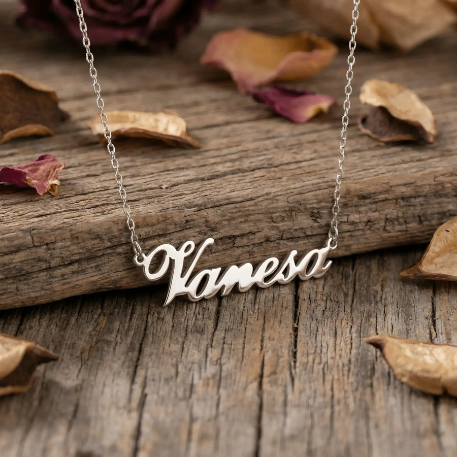 Lănțișor argint 925 rodiat cu numele Vanesa, pandantiv decupat 38.5x10 mm font cursiv, lanț anchor 46 cm pe scândură de lemn vechi cu petale de trandafir uscate
