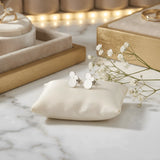 Cercei argint 925 rodiat stud cu trio cercuri pline suprapuse 11,6mm — pereche pe pernă satin crem cu placă marmură albă cu vinete gri, cutii bijuterii din lemn auriu și flori gypsophila pe fundal cu lumini bokeh aurii, finisaj oglindă alb-platinat, prindere fluturaș clasic