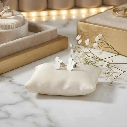 Cercei argint 925 rodiat stud cu trio cercuri pline suprapuse 11,6mm — pereche pe pernă satin crem cu placă marmură albă cu vinete gri, cutii bijuterii din lemn auriu și flori gypsophila pe fundal cu lumini bokeh aurii, finisaj oglindă alb-platinat, prindere fluturaș clasic