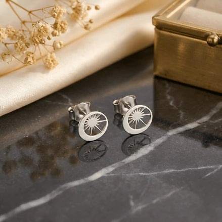 Cercei argint 925 rodiat stud cu compoziție soare-lună 10x10mm — pereche pe placă de marmură neagră lăcuită cu pânză mătăsoasă crem și ramuri uscate gypsophila, soare cu raze decupate pe dreapta, semilună plină pe stânga, finisaj oglindă alb-platinat