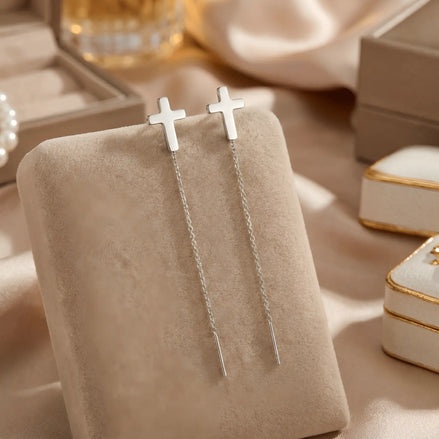 Cercei argint 925 rodiat threader cu cruce latină mică 6,5mm — pereche pe pernă velvet bej cu draperie satin crem și cutii de bijuterii cu margini aurii în fundal, lanț subțire 6cm cu tijă-bară, finisaj oglindă alb-platinat