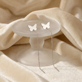 Cercei argint 925 rodiat threader cu fluture plin stilizat 7,5mm — pereche pe suport rotund de sticlă mată cu drape velvet crem-bej, aripi pline simetrice, corp central subțire, lanț 6cm cu tijă-bară, finisaj oglindă alb-platinat