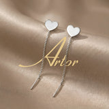 Cercei argint 925 rodiat threader cu inimă plină 8mm — pereche pe satin auriu cu logo Artor pe fundal, inimă singulară pe vârf, lanț subțire 6cm cu tijă-bară, finisaj oglindă alb-platinat