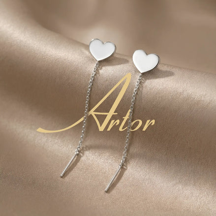 Cercei argint 925 rodiat threader cu inimă plină 8mm — pereche pe satin auriu cu logo Artor pe fundal, inimă singulară pe vârf, lanț subțire 6cm cu tijă-bară, finisaj oglindă alb-platinat