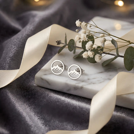 Cercei argint 925 rodiat stud cu munte în cerc outline 8,6mm — pereche pe placă marmură albă pe drape velvet gri-grafit cu satin auriu și lumini bokeh aurii pe fundal, ramuri eucalipt și flori gypsophila în spate, finisaj oglindă alb-platinat, prindere fluturaș clasic