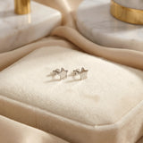 Cercei argint 925 rodiat stud cu stea mică plină 6mm — pereche pe pernă din velvet crem cu draperie satin pe fundal, accente de marmură albă cu detalii aurii, finisaj oglindă alb-platinat, prindere fluturaș clasic