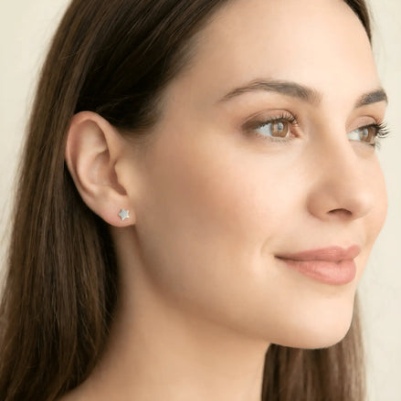 Cercei argint 925 rodiat stud cu stea plină 6mm — purtată pe lobul urechii drepte de model brunet cu păr lung, vârful stelei orientat în sus, ten luminos, cadru lifestyle damă