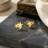 Cercei aur 14K stud trio stele stilizate 11.5x10mm — vedere produs cu trei stele aliniate pe arc curbat, finisaj oglindă pe marmură neagră
