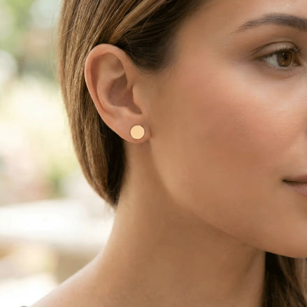 Cercei aur 14K bănuț plin purtați pe ureche — model dama cu părul prins, disc rotund minimalist lângă obraz în lumină naturală