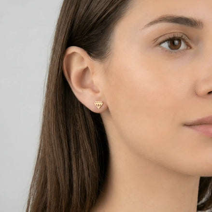 Cercei aur 14K diamant stilizat purtați pe ureche — model dama păr brunet, formă diamant cu fațete decupate vizibile pe lobul urechii
