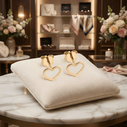 Cercei aur 14K stud cu inimă contur outline — pereche pe pernă crem cu fundal boutique, două inimi cu margine subțire și mijloc decupat, finisaj oglindă, prindere fluturaș push-back, dimensiune 9x8mm