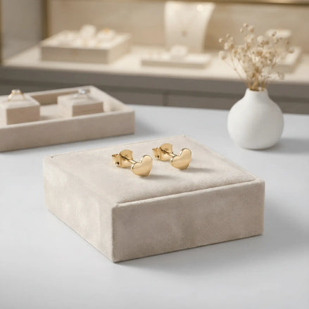 Cercei aur 14K stud cu inimă mică plină 6x6mm — pereche pe pernuță de catifea crem, vitrină cu bijuterii și flori uscate gypsophila pe fundal, finisaj oglindă, prindere fluturaș push-back