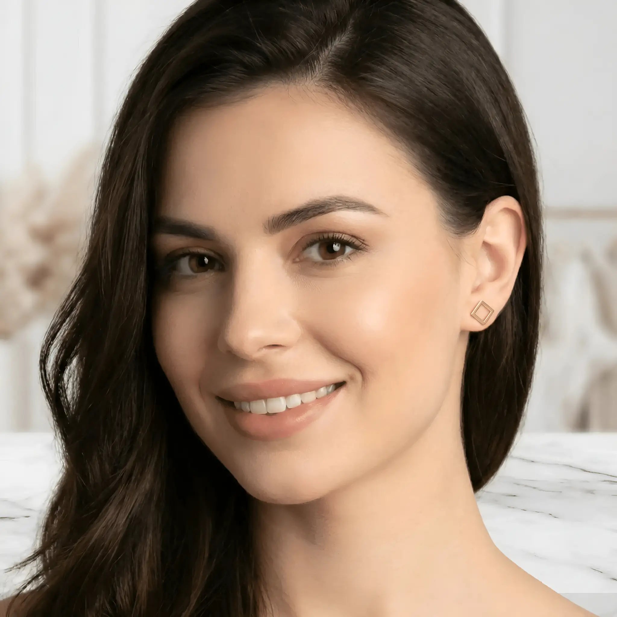 Cercei aur 14K stud pătrat outline — purtată pe lobul urechii unei tinere brunete cu păr lung, pătrățel mic vizibil, ten clar, fundal alb minimalist