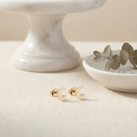 Cercei aur 14K stud semilună crai-nou — pereche pe textil ivory cu eucalipt uscat și platou de marmură, două semilune subțiri lustruite oglindă, dimensiune 9x7mm