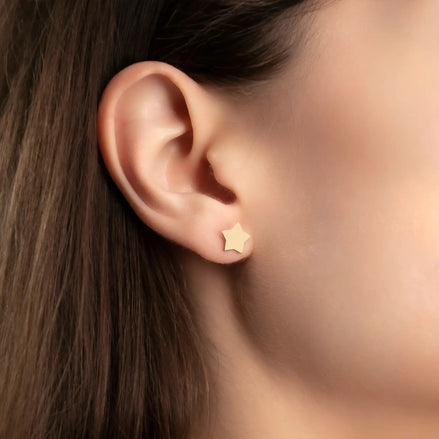 Cercei aur 14K stud stea — purtată pe lobul urechii unei tinere brunete, steaua mare vizibilă clar pe ureche, păr lung castaniu cădere natural pe lateral