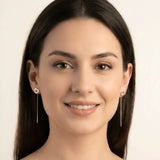 Cercei aur 14K threader inimă contur purtați pe ureche — model dama păr brunet zâmbind, conturul subțire al inimii deasupra lobului, lănțișor pe spate