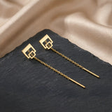 Cercei aur 14K threader cu dublu pătrat outline 9,3mm — pereche pe placă piatră ardezie neagră cu drape satin auriu pe fundal, pătrat mare sus și pătrat mic atașat în jos cu interior gol, lanț 6cm cu tijă-bară, finisaj oglindă pe aur galben