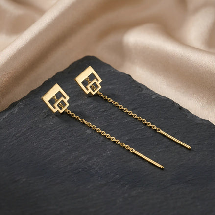 Cercei aur 14K threader cu dublu pătrat outline 9,3mm — pereche pe placă piatră ardezie neagră cu drape satin auriu pe fundal, pătrat mare sus și pătrat mic atașat în jos cu interior gol, lanț 6cm cu tijă-bară, finisaj oglindă pe aur galben