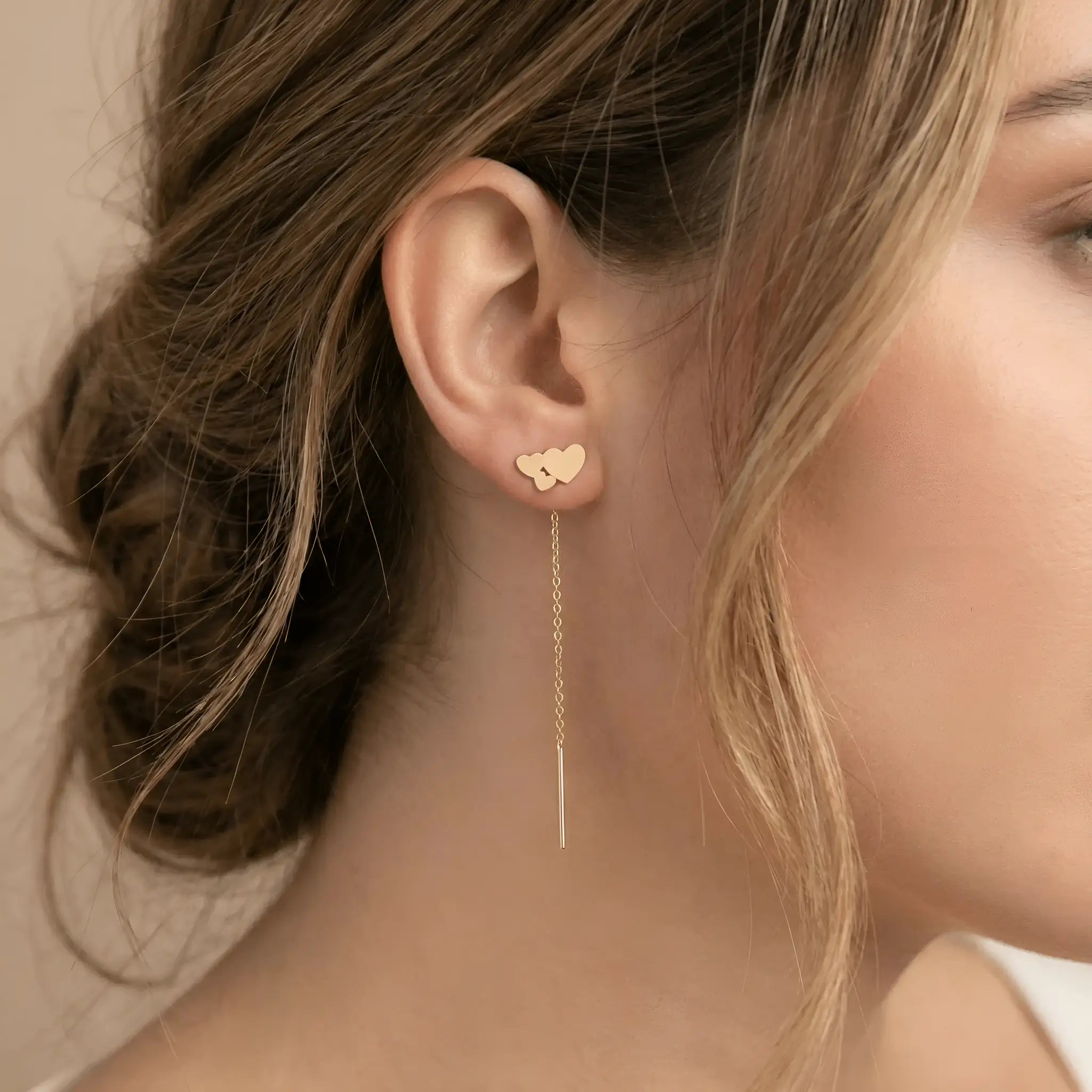 Cercei aur 14K threader trio inimi purtați pe ureche — model dama păr blond, compoziție trei inimi suprapuse deasupra lobului, lănțișor lung pe spate