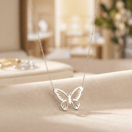 Lănțișor argint 925 rodiat cu pandantiv fluture cu aripile larg desfăcute și motive decupate fin pe lanț subțire alb-platinat, ambianță atelier crem