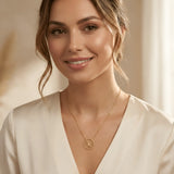 Damă tânără purtând colier aur 14K cu pandantiv Floarea Vieții pe top crem cu decolteu V, lumină caldă de interior cu drapaj satinat