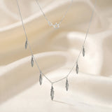 Lănțișor choker argint 925 rodiat cu 7 pandantive pene mici antichizate distribuite simetric pe lanț subțire alb-platinat, ambianță textilă crem
