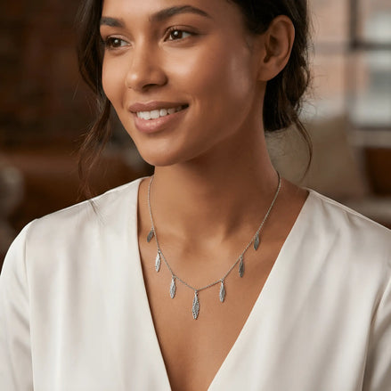 Damă tânără purtând choker argint 925 rodiat cu 7 pandantive pene, peste bluză albă cu decolteu V adânc, lumină naturală caldă, atmosferă urban-boho