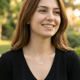 Damă tânără purtând lănțișor argint 925 rodiat cu numele Ada script, peste top negru cu decolteu V, lumină naturală exterior cu vegetație