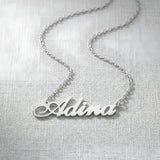 Lănțișor argint 925 rodiat personalizat cu numele Adina decupat în scriere cursivă elegantă cu coadă caligrafică pe textil alb țesut, lanț subțire alb-platinat