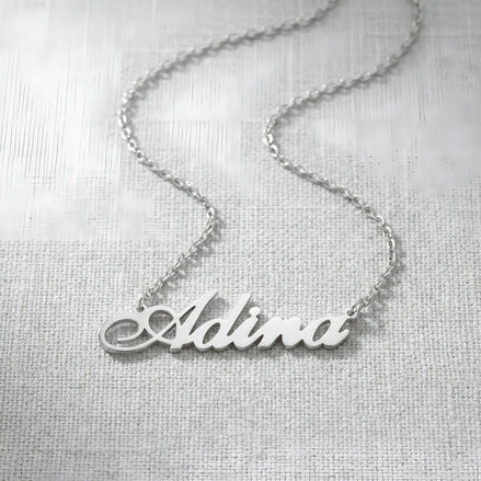 Lănțișor argint 925 rodiat personalizat cu numele Adina decupat în scriere cursivă elegantă cu coadă caligrafică pe textil alb țesut, lanț subțire alb-platinat