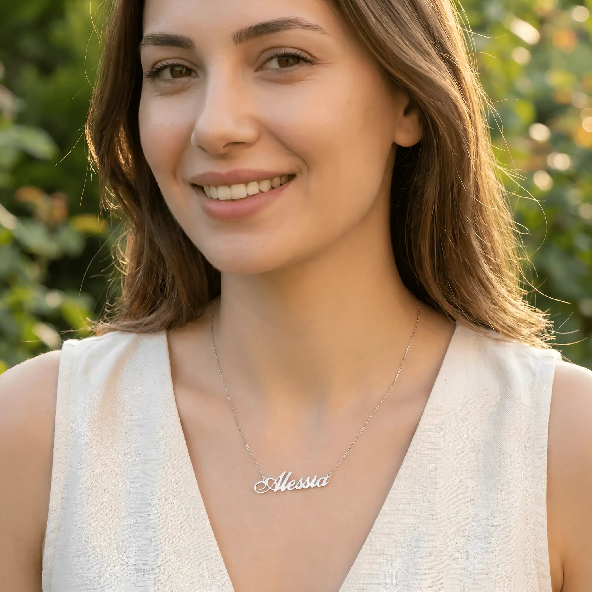 Damă tânără purtând lănțișor argint 925 rodiat cu numele Alessia, peste top alb din in deshumeral cu V, lumină naturală caldă în exterior
